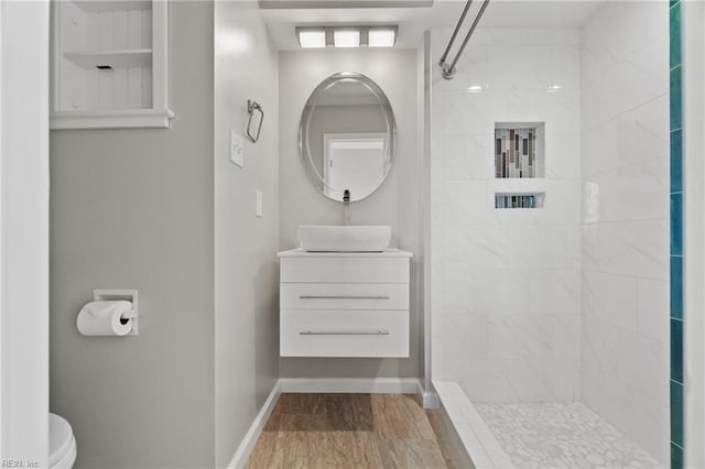 full bath featuring toilet, a tile shower, vanity, wood finished floors, and baseboards