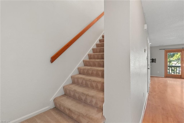 stairs featuring a textured ceiling, wood finished floors, and baseboards