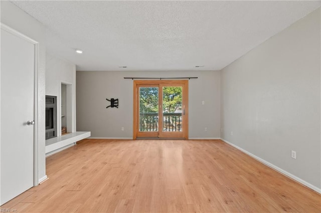 empty room featuring a fireplace with raised hearth, light wood finished floors, a textured ceiling, and baseboards