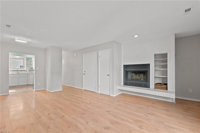 unfurnished living room featuring baseboards, a fireplace with raised hearth, visible vents, and light wood finished floors