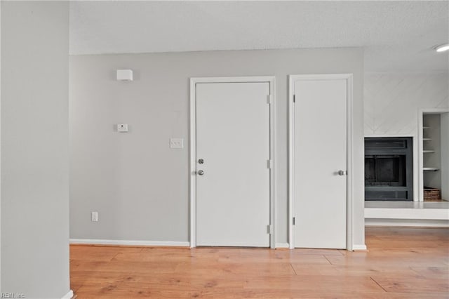 interior space with light wood-type flooring, a fireplace, a textured ceiling, and baseboards