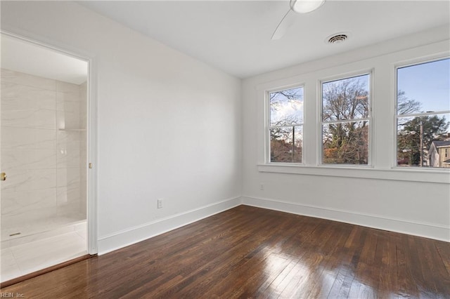 empty room featuring dark wood-style flooring, visible vents, and baseboards