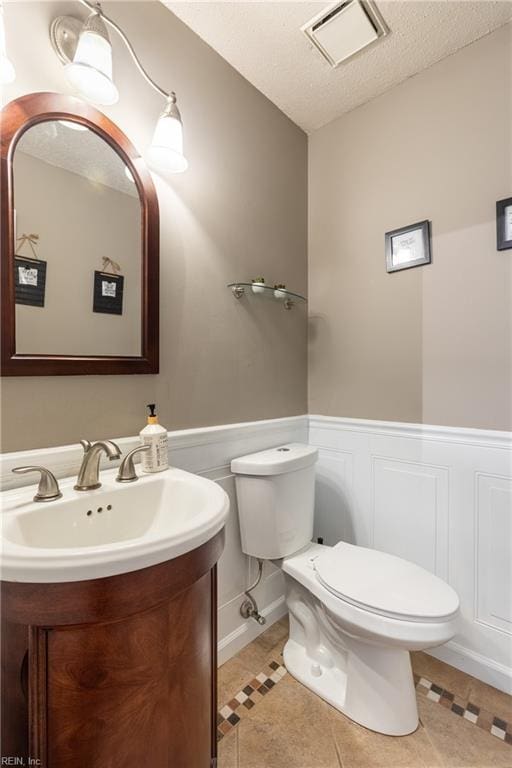 bathroom featuring visible vents, wainscoting, toilet, a textured ceiling, and vanity