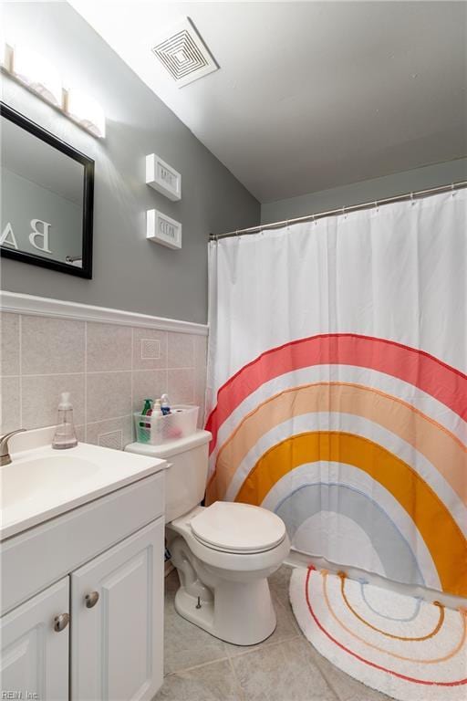 bathroom with visible vents, toilet, tile patterned flooring, vanity, and tile walls