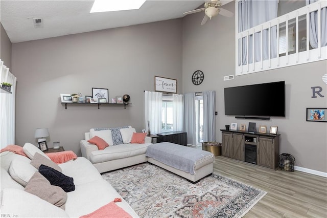 living area featuring a skylight, a high ceiling, a ceiling fan, wood finished floors, and baseboards