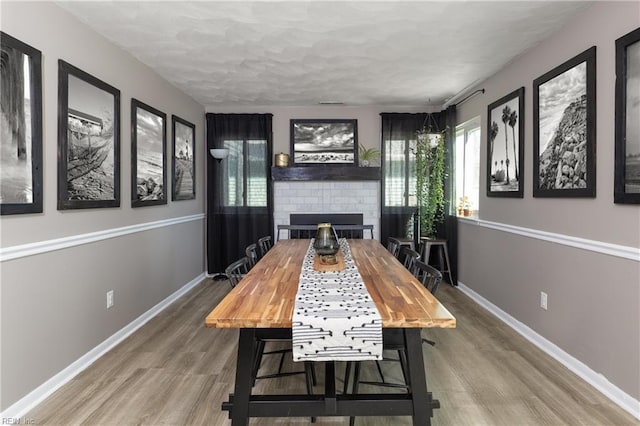 dining room featuring a brick fireplace, baseboards, and wood finished floors