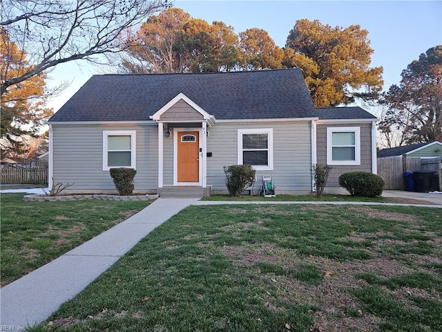 view of front of house featuring roof with shingles, fence, and a front lawn