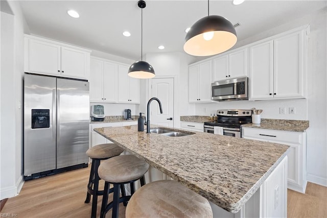 kitchen with stainless steel appliances, light wood-type flooring, a sink, and a center island with sink