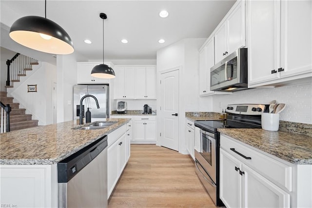 kitchen with appliances with stainless steel finishes, white cabinets, a sink, and light wood-style flooring