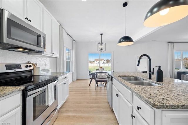 kitchen with stainless steel appliances, a sink, white cabinetry, light wood-style floors, and backsplash