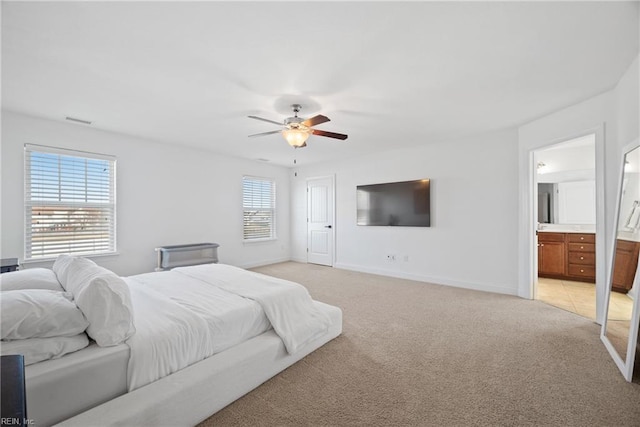 bedroom with ceiling fan, ensuite bathroom, light colored carpet, visible vents, and baseboards