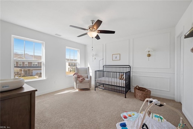 carpeted bedroom with ceiling fan, a crib, visible vents, and a decorative wall