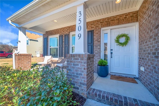 doorway to property with a porch and brick siding