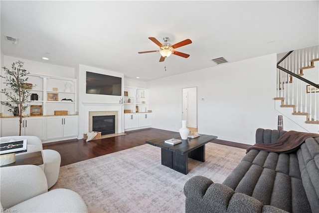 living room with visible vents, a ceiling fan, a fireplace with flush hearth, dark wood-type flooring, and stairs