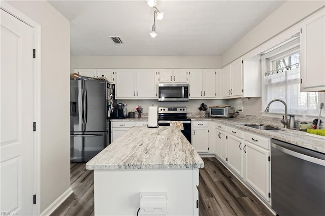 kitchen featuring appliances with stainless steel finishes, white cabinets, a sink, and a center island