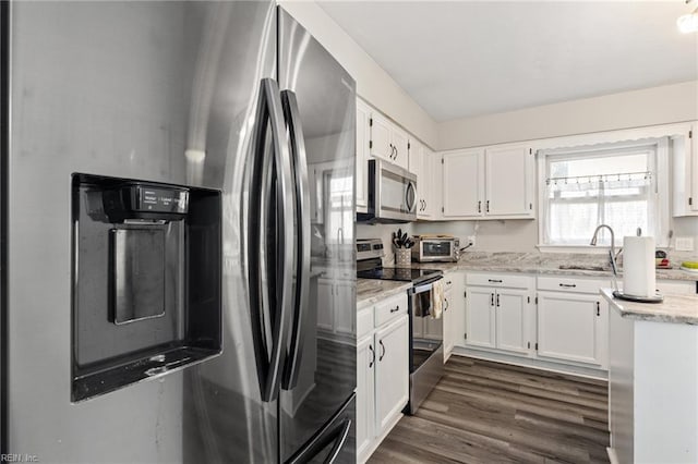 kitchen with light stone counters, dark wood-style flooring, a sink, white cabinetry, and appliances with stainless steel finishes