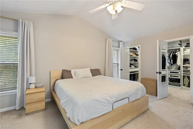 carpeted bedroom with a ceiling fan, a walk in closet, vaulted ceiling, and baseboards