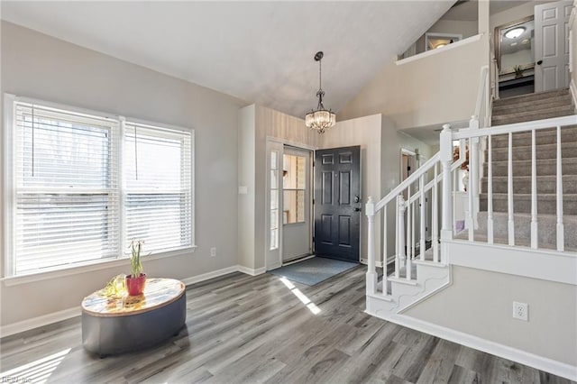 entrance foyer with an inviting chandelier, wood finished floors, high vaulted ceiling, baseboards, and stairs