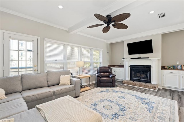 living area featuring crown molding, visible vents, a brick fireplace, wood finished floors, and beamed ceiling