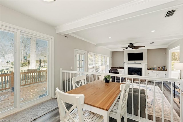 dining area with ceiling fan, a fireplace, visible vents, ornamental molding, and beam ceiling