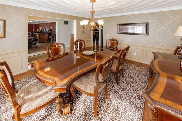 dining area with a wainscoted wall, crown molding, an inviting chandelier, and wallpapered walls