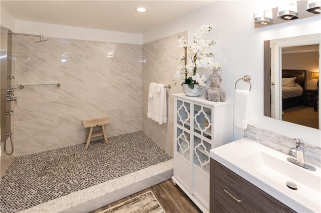 ensuite bathroom featuring decorative backsplash, connected bathroom, tiled shower, wood finished floors, and vanity