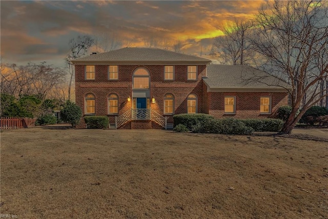 colonial house with brick siding, a front yard, and fence