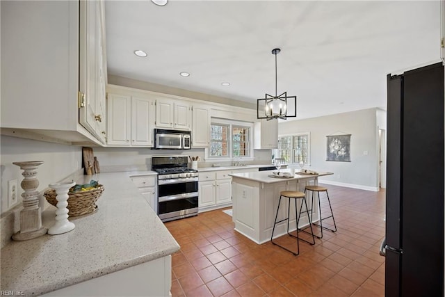 kitchen featuring stainless steel appliances, a sink, white cabinets, a center island, and decorative light fixtures