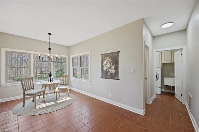 dining room featuring a chandelier, dark tile patterned flooring, washer / clothes dryer, and baseboards