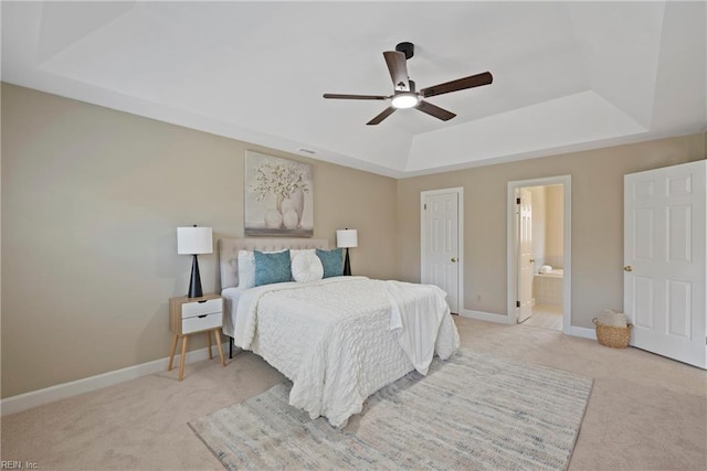 bedroom with light carpet, baseboards, a tray ceiling, and ensuite bathroom