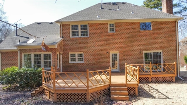 rear view of property with roof with shingles, brick siding, a chimney, and a wooden deck