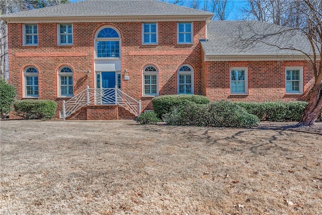 colonial-style house featuring brick siding and a shingled roof