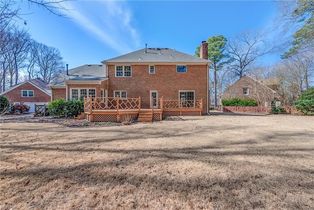 back of property featuring a deck, brick siding, a yard, and a chimney