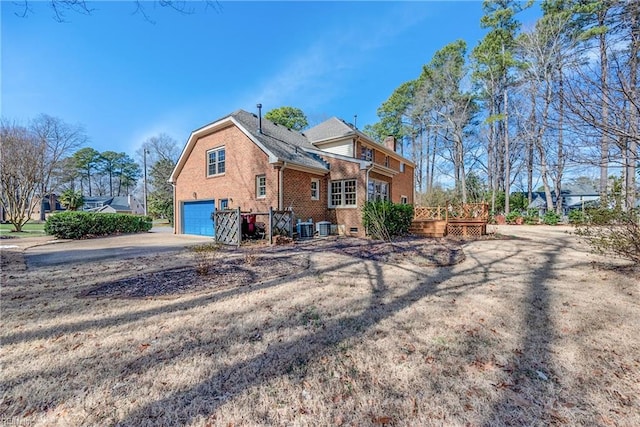 rear view of property with brick siding, a chimney, concrete driveway, an attached garage, and a wooden deck