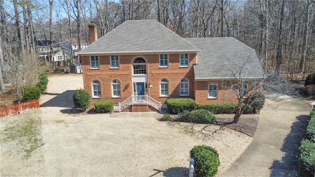 view of front facade featuring dirt driveway, a chimney, roof with shingles, fence, and brick siding