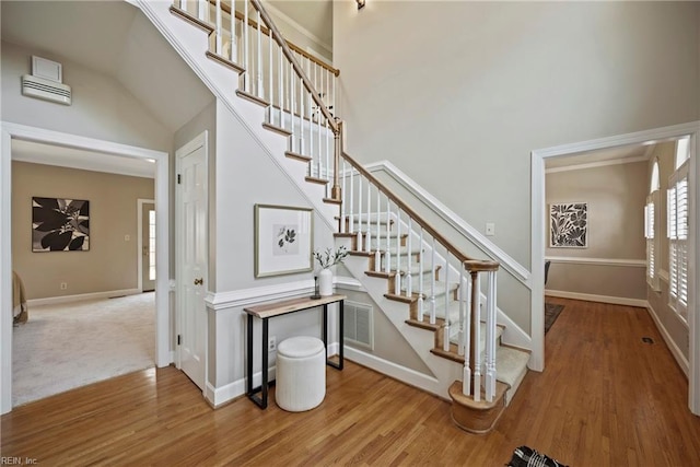 stairs featuring a high ceiling, wood finished floors, visible vents, and baseboards