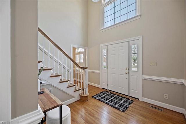 entrance foyer with a high ceiling, wood finished floors, visible vents, baseboards, and stairs