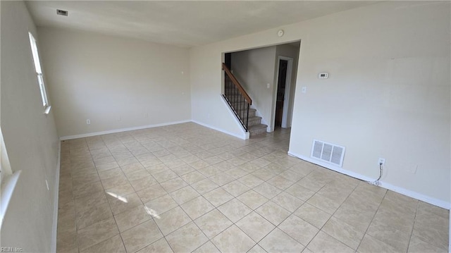 spare room featuring stairs, light tile patterned floors, visible vents, and baseboards