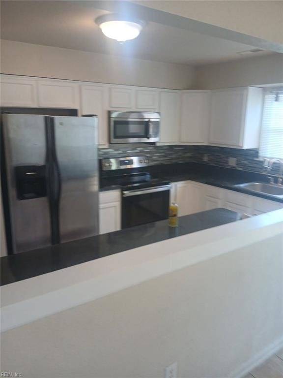 kitchen featuring stainless steel appliances, white cabinets, a sink, and backsplash