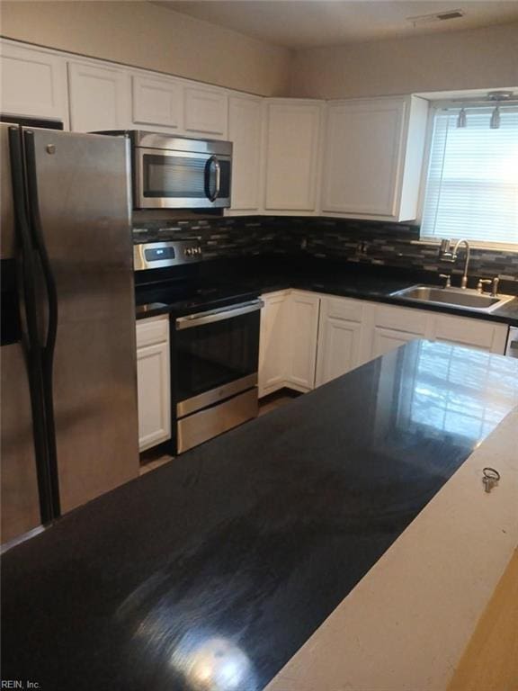 kitchen featuring appliances with stainless steel finishes, white cabinetry, a sink, and backsplash