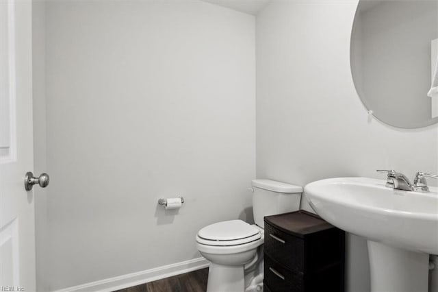 bathroom featuring toilet, a sink, baseboards, and wood finished floors