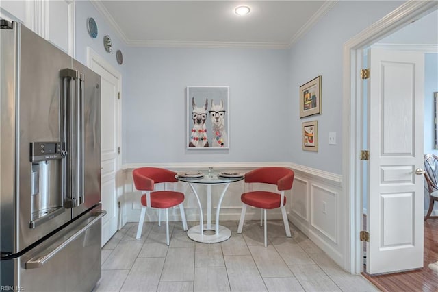 dining space with a wainscoted wall, breakfast area, a decorative wall, ornamental molding, and light tile patterned flooring