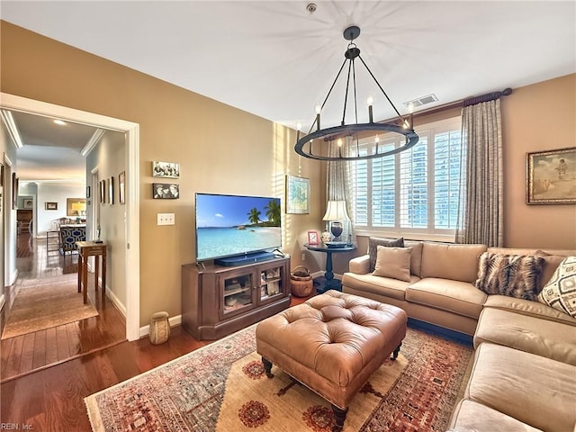 living area featuring a notable chandelier, wood finished floors, visible vents, baseboards, and crown molding