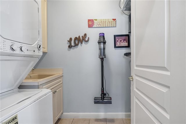 laundry area featuring light tile patterned floors, stacked washer / dryer, cabinet space, and baseboards