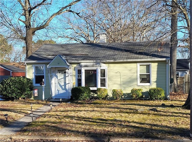 bungalow-style home featuring a shingled roof, a chimney, fence, and a front lawn