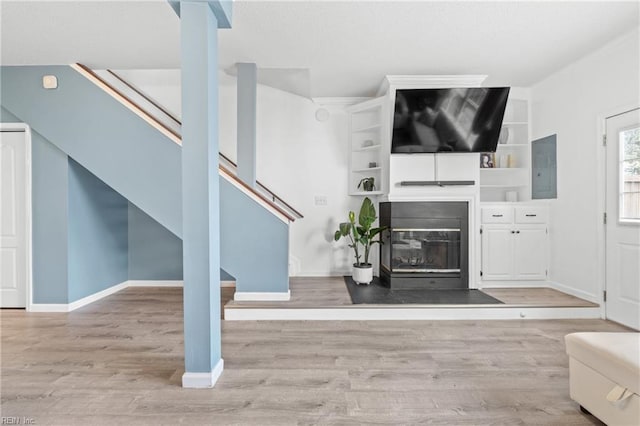 unfurnished living room featuring a fireplace with flush hearth, stairs, baseboards, and wood finished floors