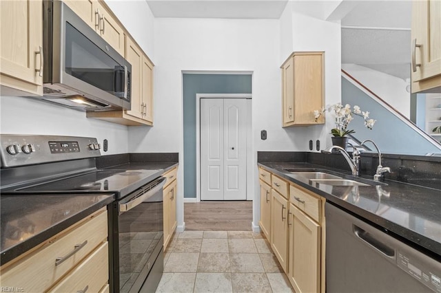 kitchen with baseboards, dark stone counters, appliances with stainless steel finishes, light brown cabinetry, and a sink