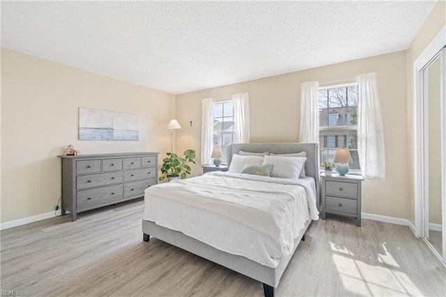 bedroom with baseboards, multiple windows, a textured ceiling, and light wood finished floors