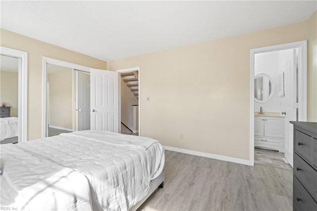 bedroom featuring ensuite bathroom, light wood-style flooring, a sink, multiple closets, and baseboards