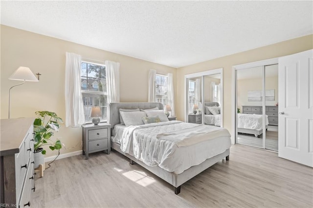 bedroom with light wood-style floors, a textured ceiling, baseboards, and two closets